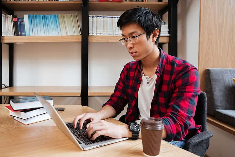 Man using laptop at the library and drinking coffee