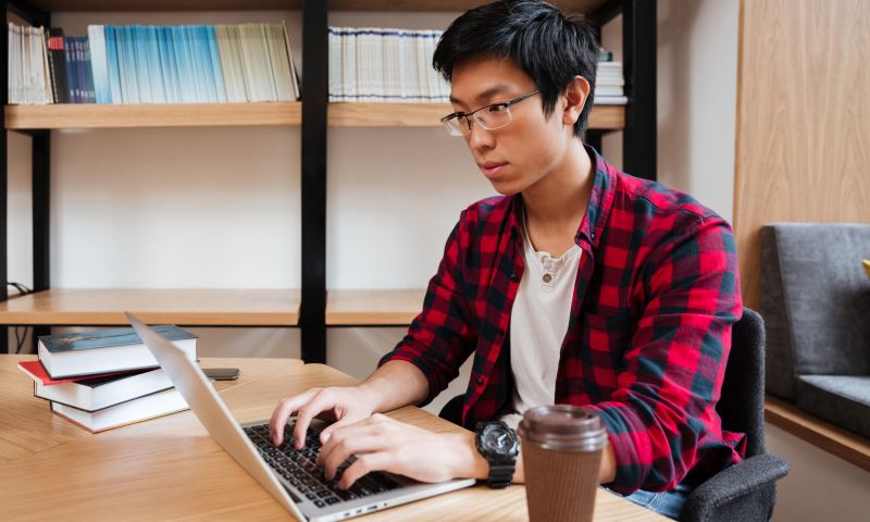 Man using laptop at the library and drinking coffee