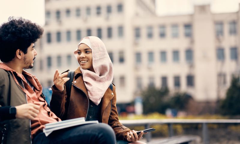 Happy Muslim college couple communicating while relaxing outdoors.