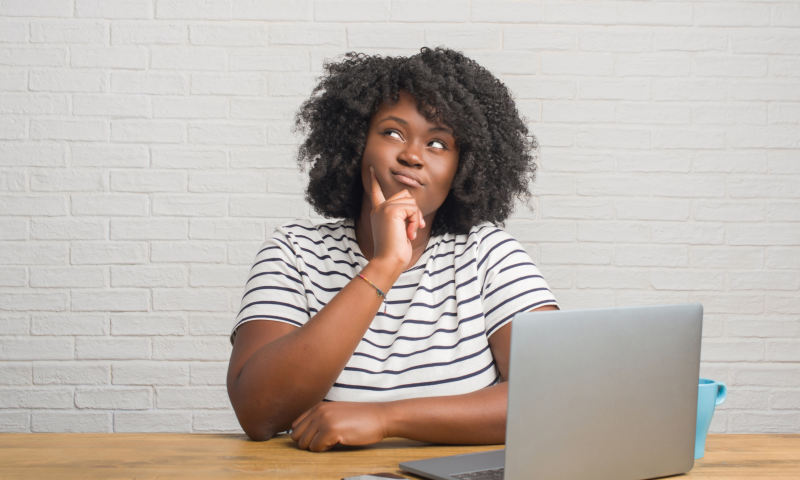 Young african american woman sitting on the table using computer laptop serious face thinking about question, very confused idea